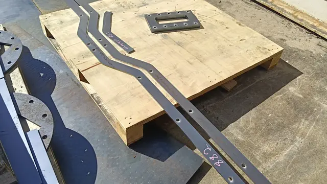 Laser-cut flat steel brackets with curved profiles on a pallet
