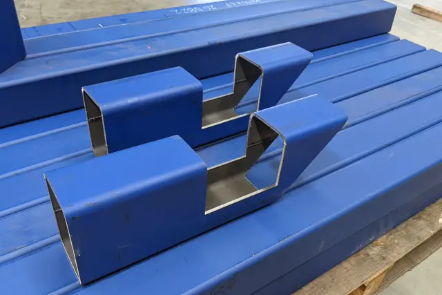 Laser-cut rectangular steel tube sections with cope cuts on a pallet